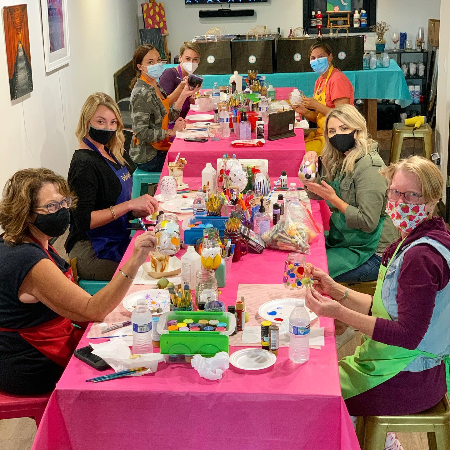 A group of people seated around a long table at a crafting party, with materials and finished crafts on the table.